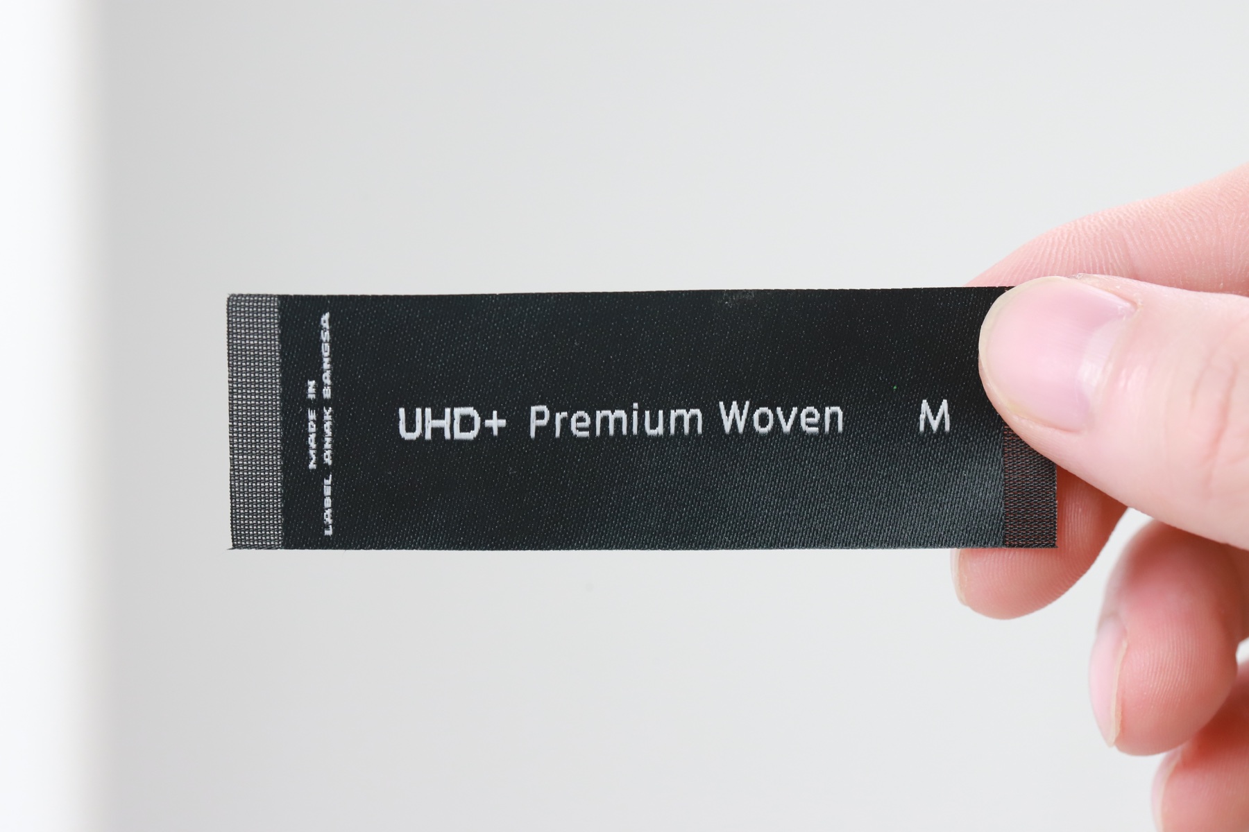 Label tenun hitam UHD+ Premium Woven dengan tulisan putih